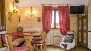 A wooden interior with a dining table, chairs, a sofa, a television, and a cabinet. - Casa Salvaniera (San Vito di Cadore)