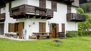 A traditional chalet with wooden balconies, a wooden bench outside, and a grassy yard. - Casa Salvaniera (San Vito di Cadore)