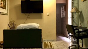 A hotel room with a bed, a desk, a chair, a TV mounted on the wall, and a lamp. - Cozy little house in São Paulo, your home away from home!!  Easy access (Unknown)