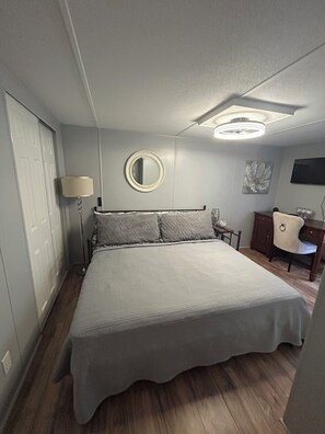 A bedroom with a bed, a bedside table, a lamp, a mirror, a dresser, and a chair.