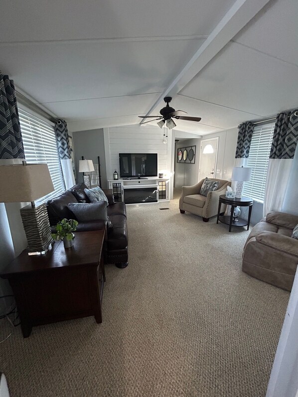 A living room with a ceiling fan, a flat-screen TV, and a fireplace. There are two sofas and a coffee table.