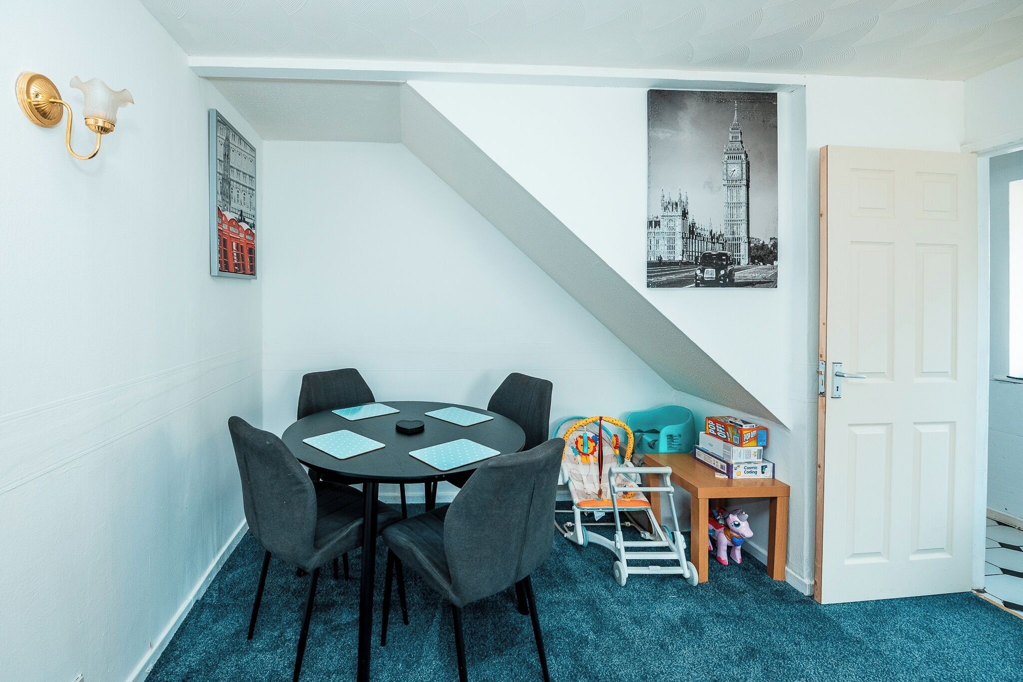 Une pièce comprenant une table à manger, des chaises, un petit espace de jeux avec des jouets et deux tableaux encadrés accrochés au mur.