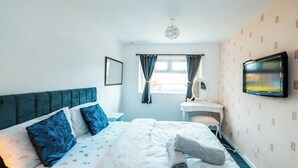 Een hotelkamer met een bed, nachtkastje, stoel, bureau, televisie en raam met gordijnen.
