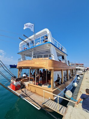 A multi-deck boat with a wooden deck, seating areas, and a flag.