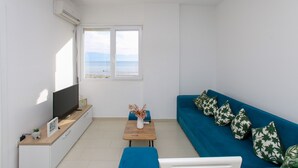 A modern living room with a large window, a flat-screen TV, a wooden coffee table, and a blue sofa with patterned cushions.