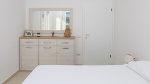 A bedroom with a bed, a dresser with drawers, a mirror, and a door.
