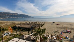 A beach with thatched-roof huts, a clear view of the sea, and distant mountains.
