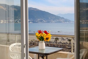 Ein Balkon mit Tisch und Stühlen, einer Vase mit Sonnenblumen und Blick auf das Meer und die Berge.