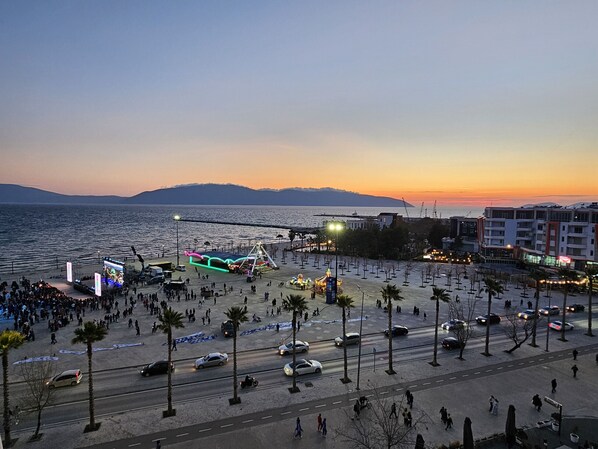 A coastal promenade with a stage, palm trees, and a road with vehicles. - Amara Sea View Apartment 7 Floor (Vlorë)