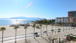 Eine Uferpromenade mit Palmen, einem Strand und Blick aufs Meer.