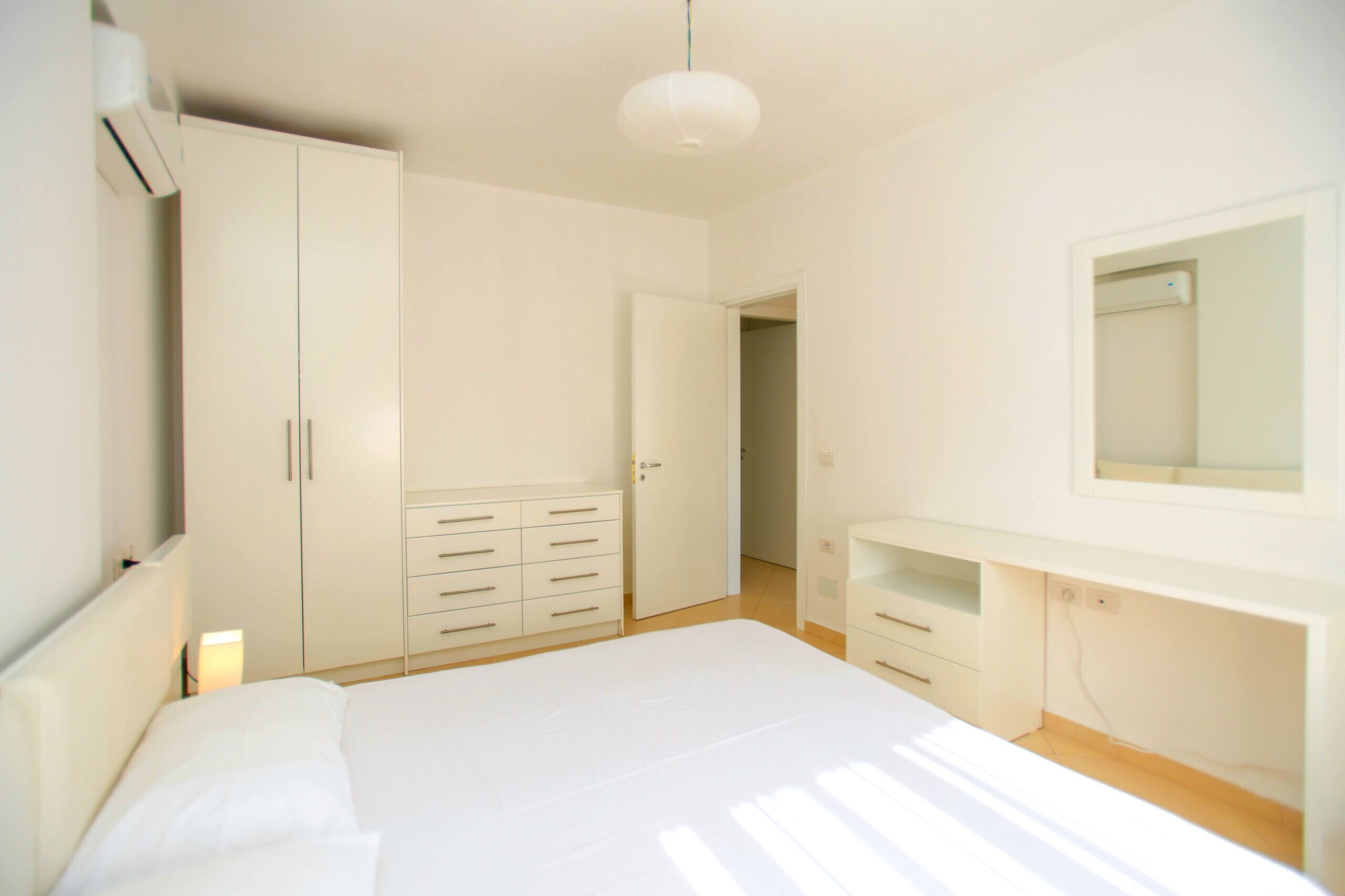A bedroom with a large bed, a wardrobe, a mirror, and a bedside table.