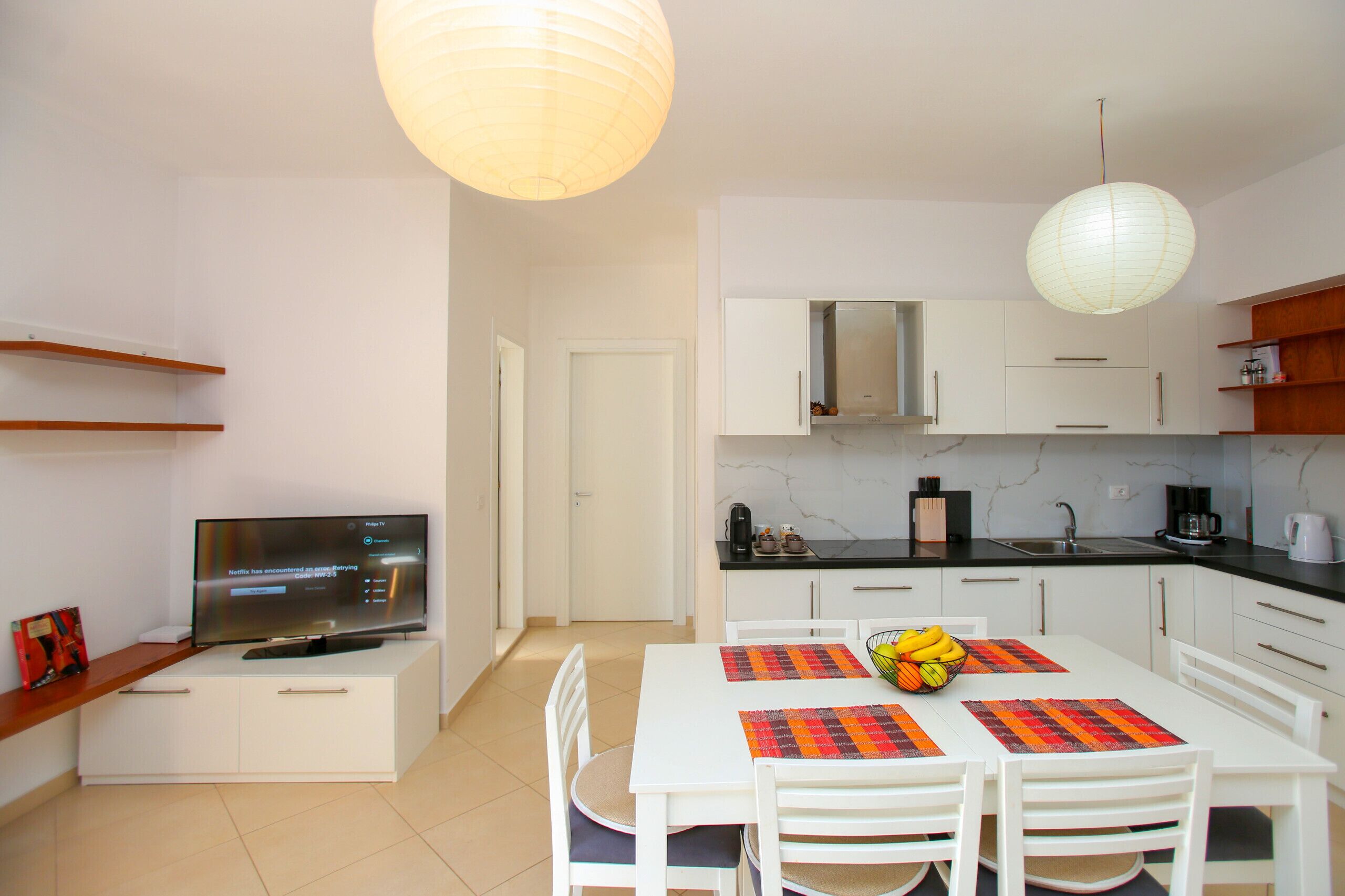 A modern kitchen with white cabinets, a black countertop, and a dining table with placemats.
