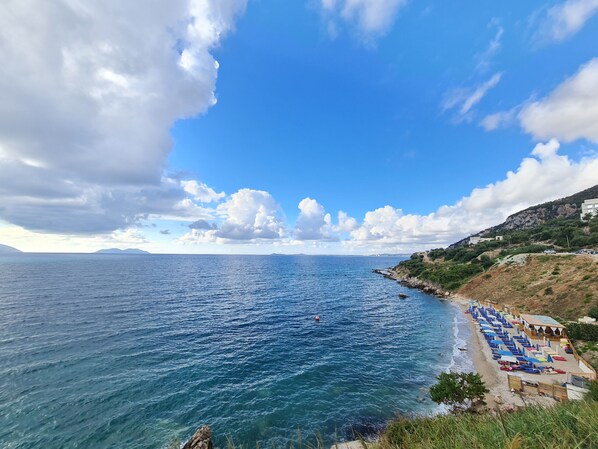 A coastal view with a beach, clear sky, and rocky terrain.
