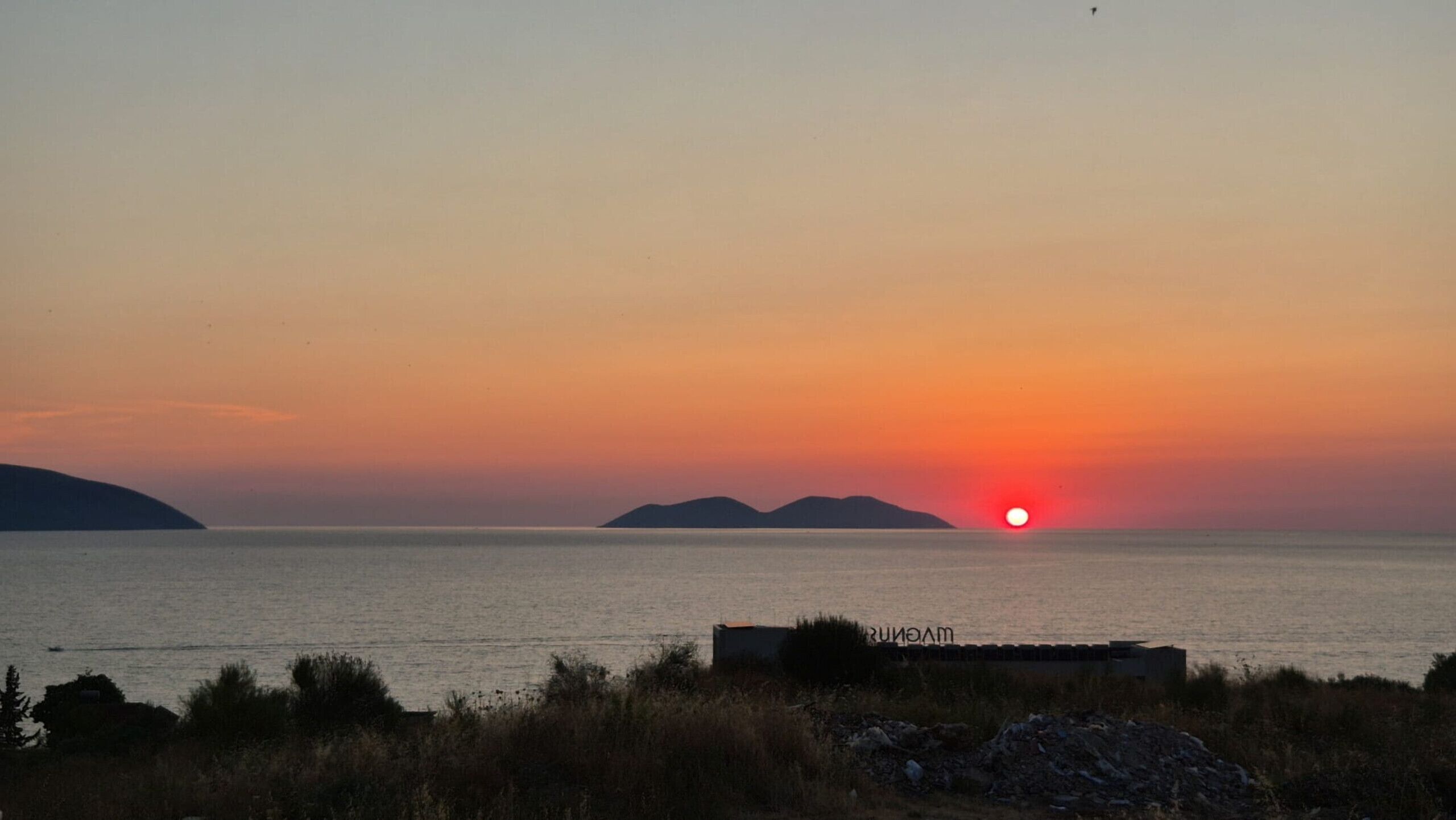 A sunset over a calm sea with distant landforms.