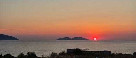 A sunset over a calm sea with distant landforms.