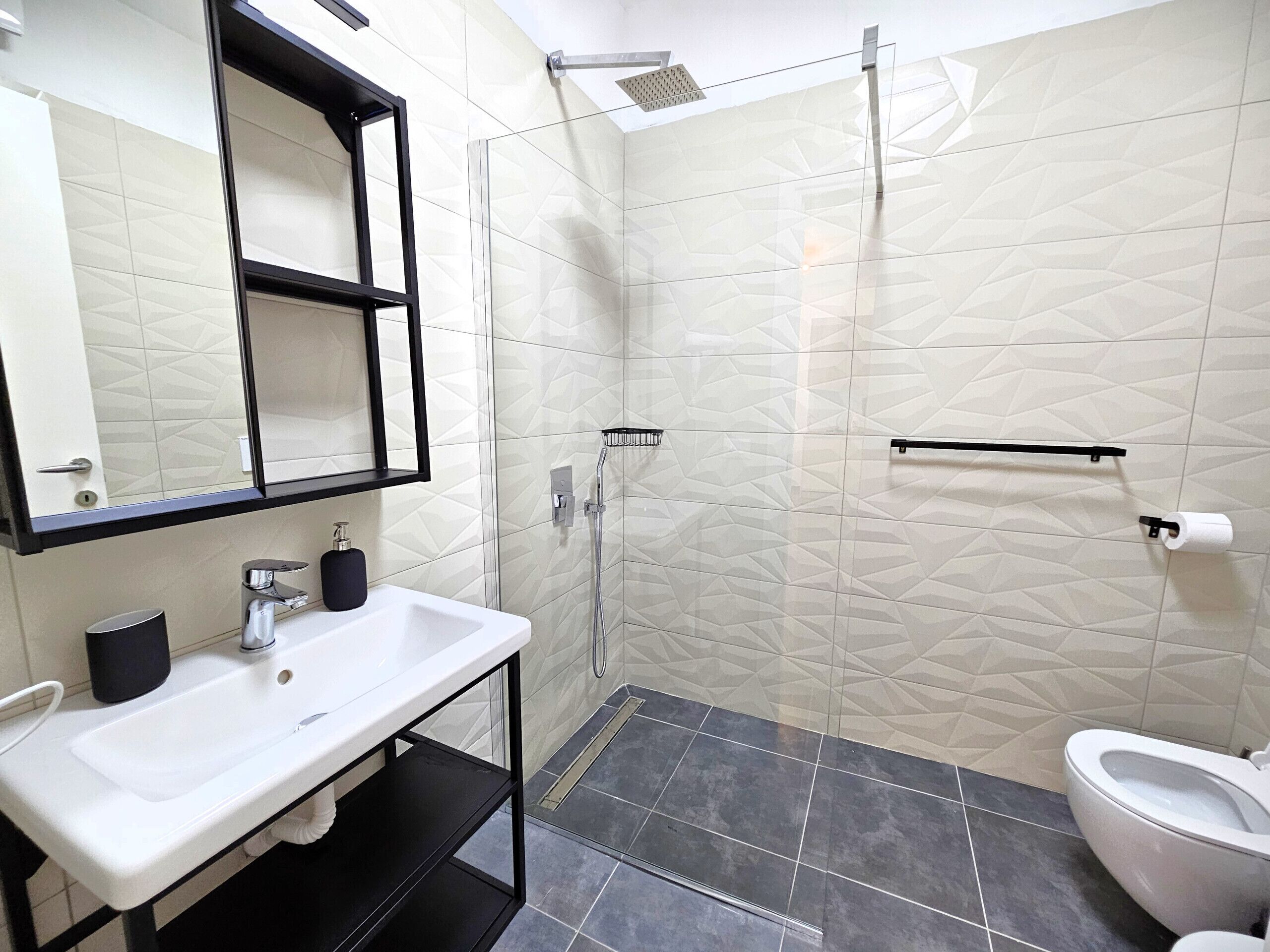 Une salle de bain moderne avec un lavabo blanc, un miroir, une douche et des toilettes.