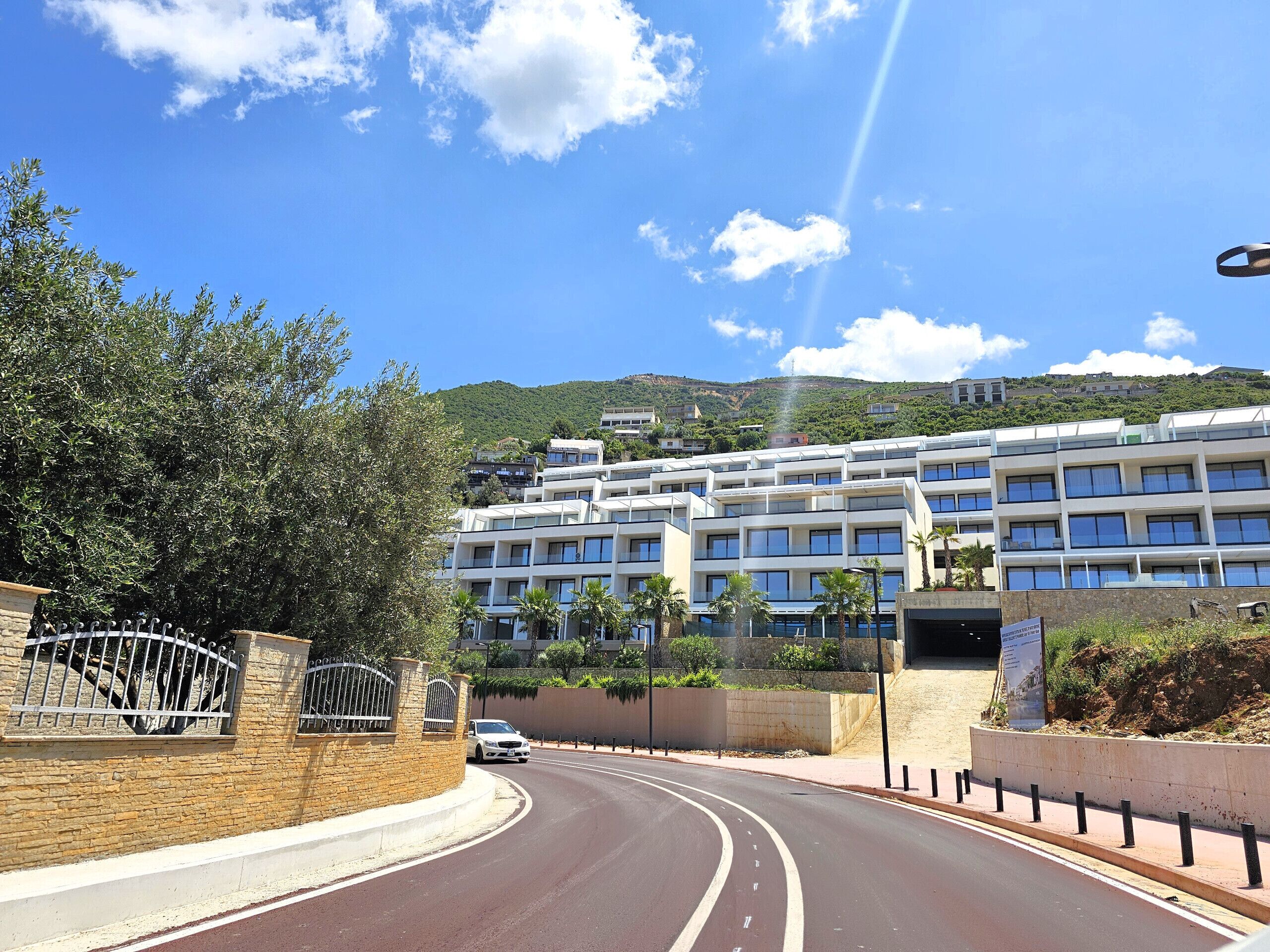 Un hôtel moderne à plusieurs étages, situé devant une route sinueuse et adossé à un paysage montagneux.