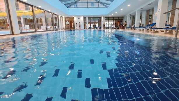 Een binnenzwembad met helderblauw water, omringd door ligbedden en een glazen dak.