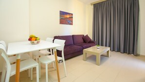 Een moderne woonkamer met een paarse bank, witte stoelen, een eettafel met fruit en een schilderij aan de muur.