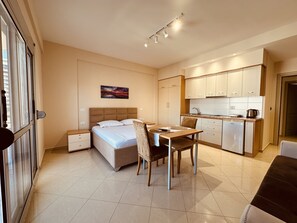 A bedroom with a bed, bedside tables, a nightstand, a dining table with chairs, a kitchen area with cabinets and a refrigerator.
