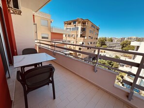 Un balcon avec une table et des chaises, une vue sur les immeubles voisins et un ciel dégagé.