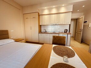 A hotel room with a bed, a dining table with placemats, a kitchen area with cabinets, and a bathroom door.