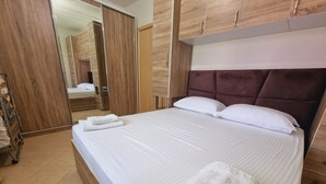 Un lit bien fait, avec du linge de lit blanc et deux serviettes pliées, une armoire en bois et un grand miroir.
