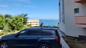 Un bâtiment moderne offrant une vue dégagée sur la mer, un VUS garé et un chemin pavé.