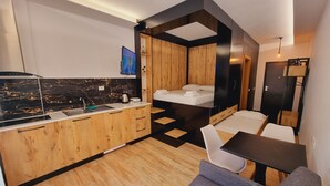 A compact hotel room with a kitchenette, a bed, a sofa, and a small dining table. - Teo's Deluxe Studios - Balcony Triple Studio (Vlorë)