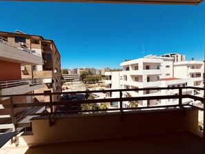 A balcony with a view of multi-story buildings, a parking area, and a clear blue sky.