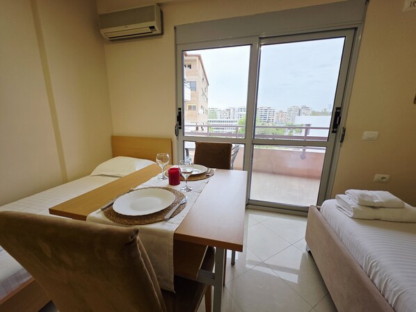 A hotel room with a bed, a table with a breakfast setup, a chair, and a view through a sliding door.