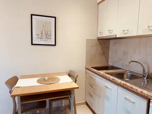 A small kitchenette with a sink, cabinets, and a dining table with chairs.