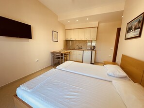A compact hotel room with a bed, a desk, and a kitchenette.