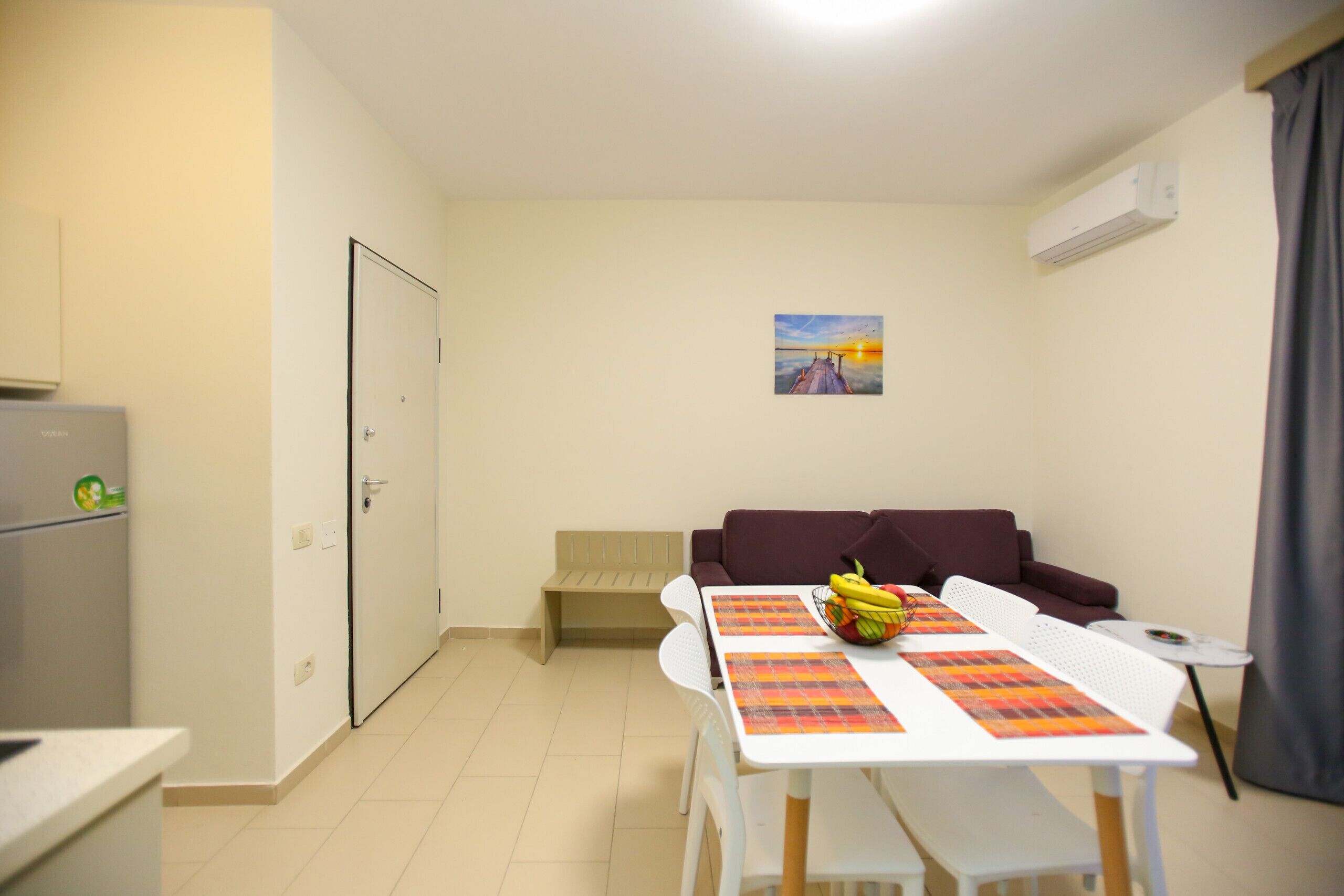 A compact living space with a kitchenette, a dining table with placemats, a sofa, and a small side table.