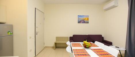 A compact living space with a kitchenette, a dining table with placemats, a sofa, and a small side table.