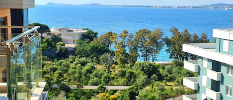 A residential area with a view of the sea, featuring modern buildings, a road with cars, and lush greenery.
