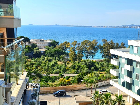 A residential area with a view of the sea, featuring modern buildings, a road with cars, and lush greenery.