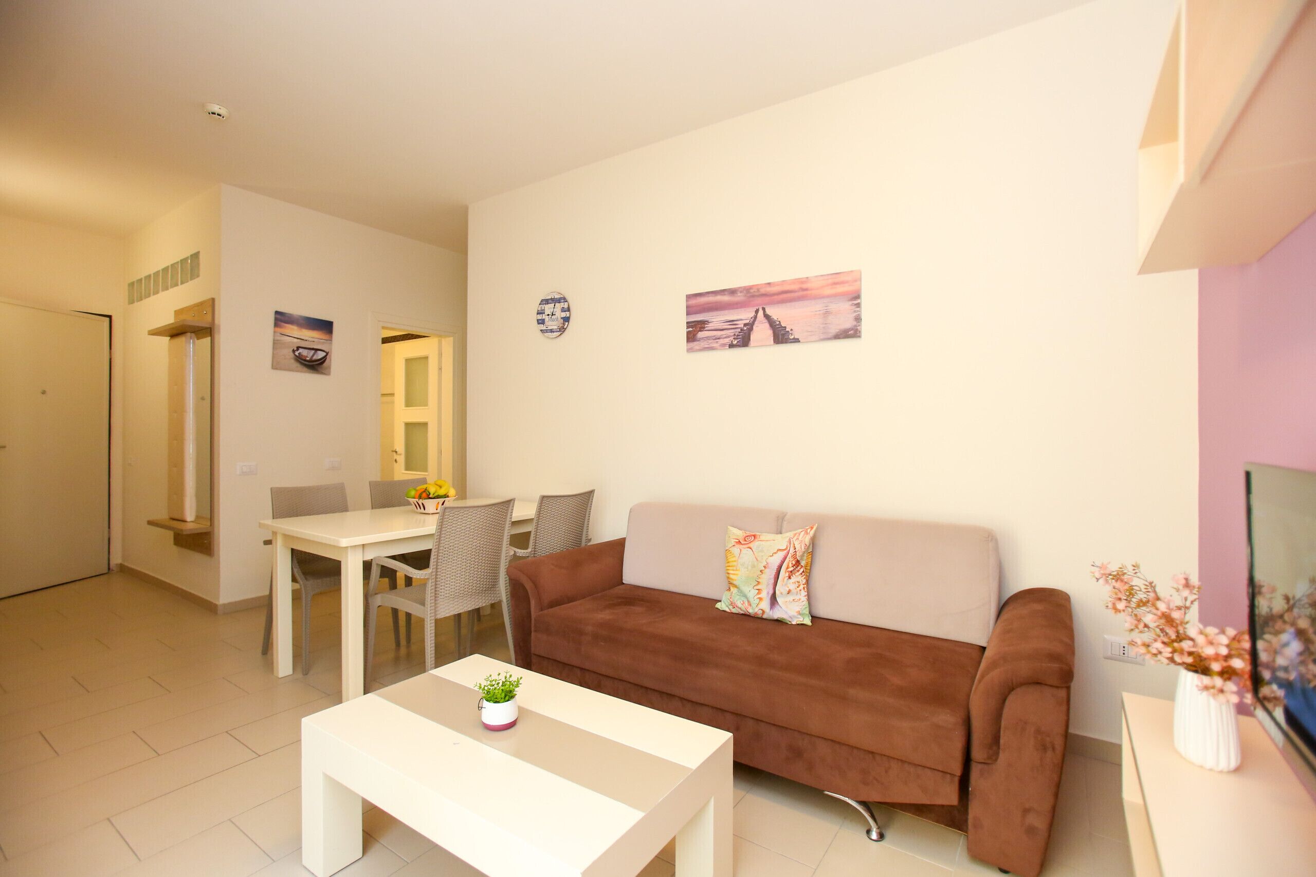 Un salon moderne avec un canapé marron, une table basse blanche et un coin repas comprenant une table et des chaises blanches.
