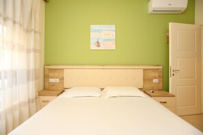 A bedroom with a bed, a nightstand, a wall-mounted air conditioner, and a door.