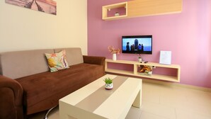 Ein Wohnzimmer mit braunem Sofa, einem weißen Couchtisch, einem an der Wand montierten Fernseher und einem Regal mit Dekoration.