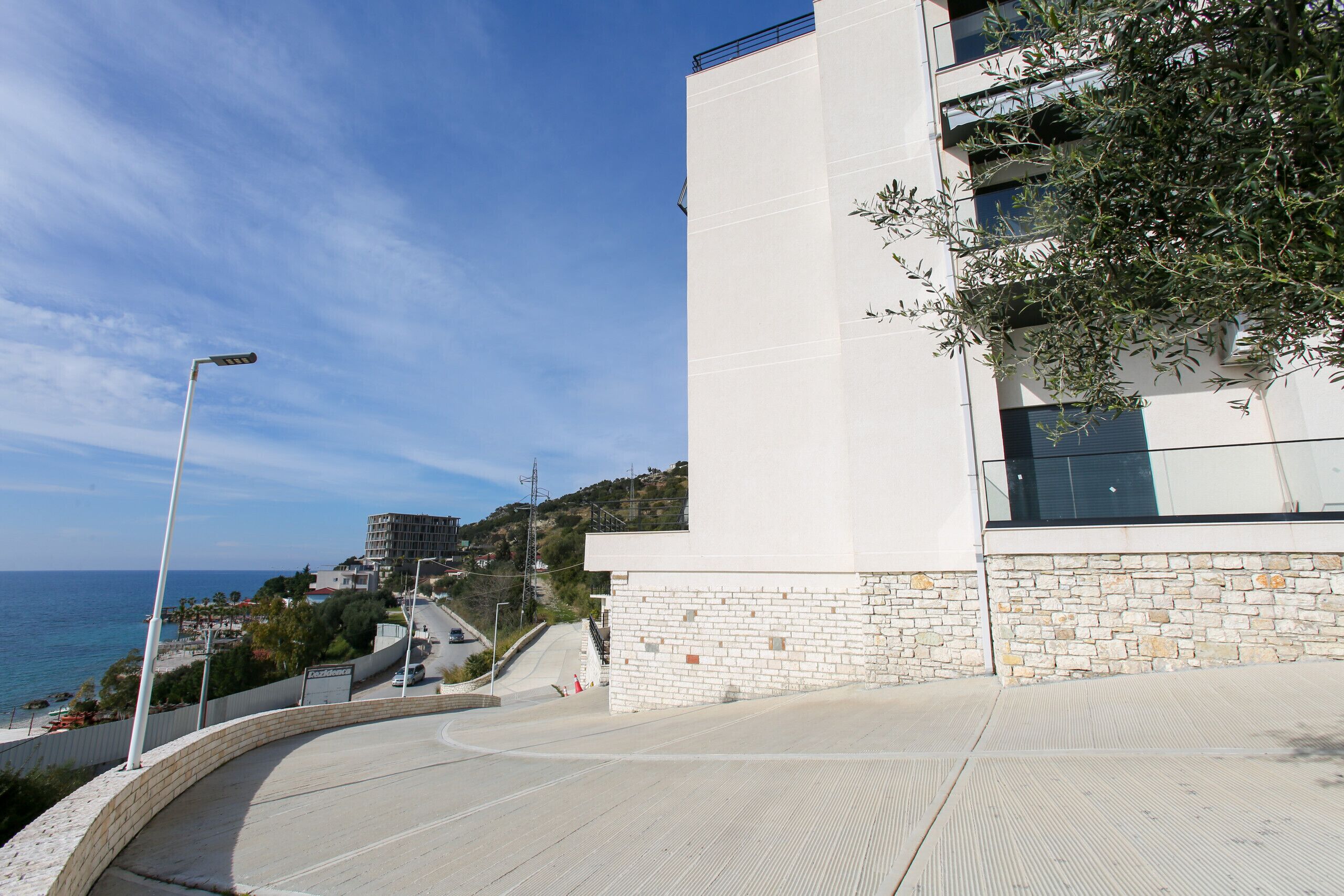 A modern building with a stone facade, a curved pathway, and a view of the sea.