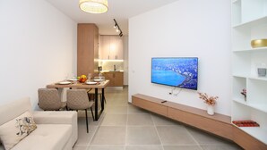 Un salon moderne doté d’un téléviseur à écran plat, d’un coin repas avec une table en bois et d’une cuisine en arrière-plan.