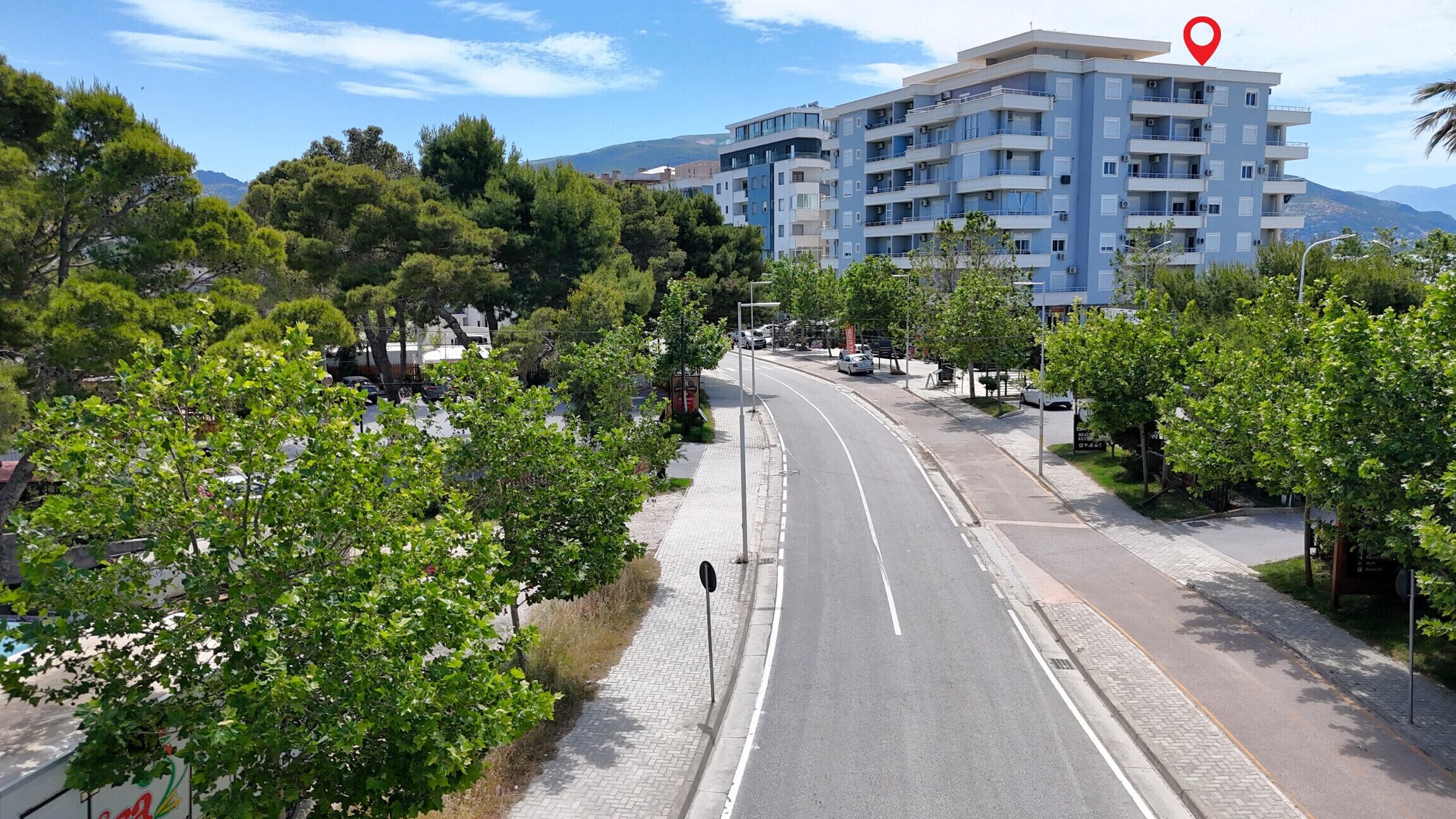 A multi-story building with a modern design, located near a road with a sidewalk and trees.