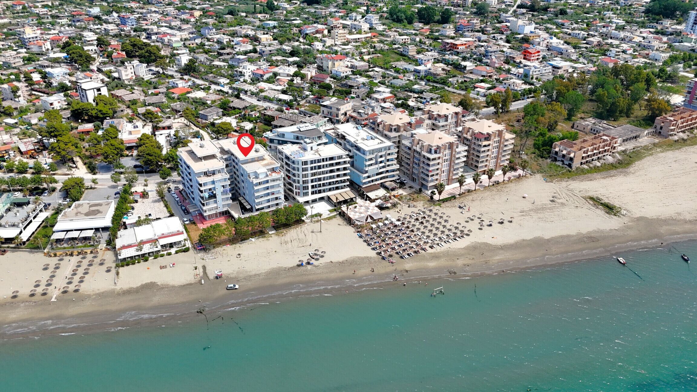 Luchtbeeld van een kuststad met een hotel aan het strand, meerdere verdiepingen, een zandstrand en helder uitzicht op zee.