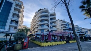 A multi-story building with balconies, a covered outdoor seating area with umbrellas, and an ATM machine.