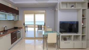 A modern kitchen with a dining area, a TV, and a balcony with a view.