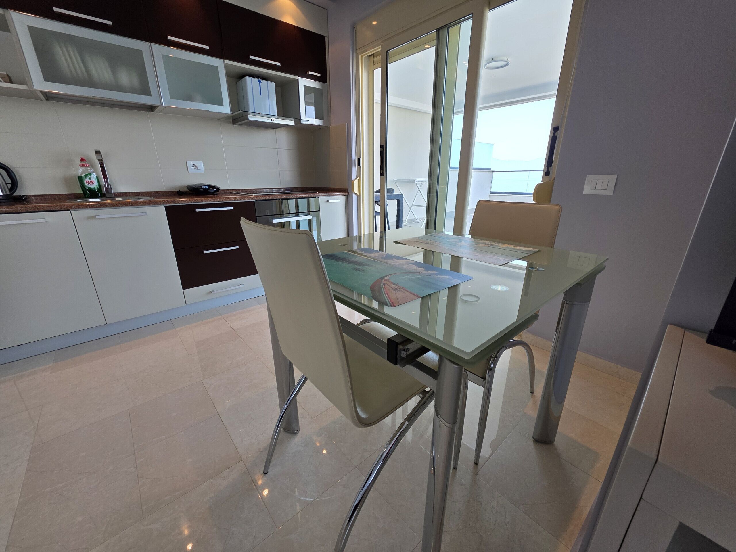A modern kitchen with dark cabinets, a microwave, and a glass dining table with chairs.