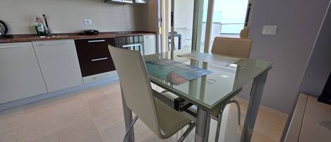 A modern kitchen with dark cabinets, a microwave, and a glass dining table with chairs.