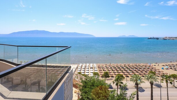 A beach view from a balcony with a clear sky, a calm sea, and a distant mountain range.
