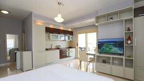 A modern hotel room with a large bed, a kitchenette, a dining area, and a TV.